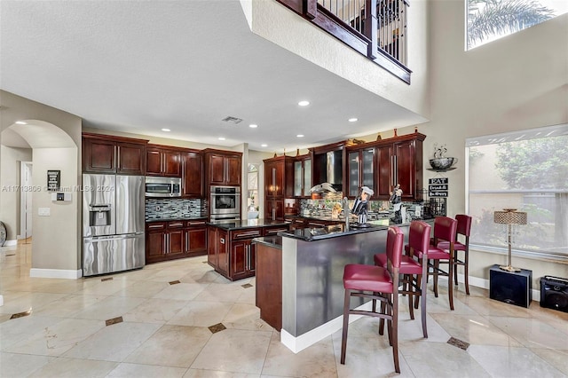 kitchen featuring decorative backsplash, appliances with stainless steel finishes, a healthy amount of sunlight, wall chimney range hood, and a kitchen island