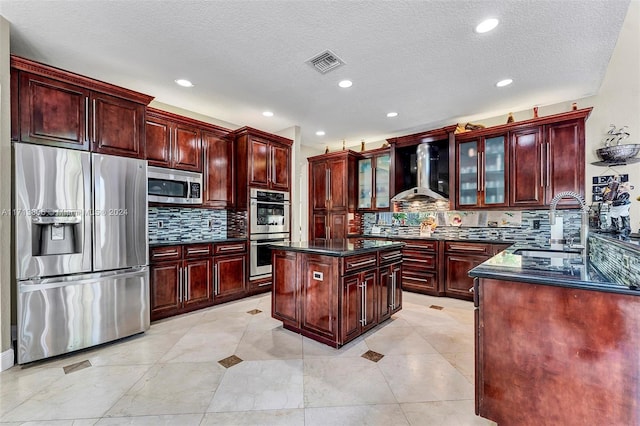 kitchen featuring wall chimney range hood, sink, decorative backsplash, appliances with stainless steel finishes, and a kitchen island