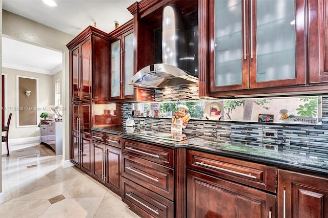 kitchen featuring wall chimney exhaust hood, backsplash, dark stone countertops, crown molding, and stainless steel gas stovetop