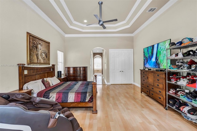 bedroom featuring ornamental molding, a tray ceiling, ceiling fan, light hardwood / wood-style flooring, and a closet