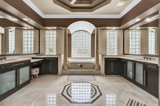 bathroom featuring a tray ceiling, tiled tub, vanity, and a healthy amount of sunlight