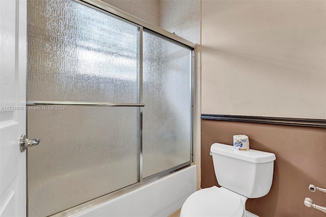 bathroom featuring toilet and combined bath / shower with glass door