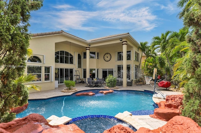 rear view of property featuring a swimming pool with hot tub and a patio area