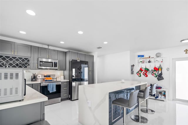 kitchen with a center island, light stone countertops, gray cabinetry, a breakfast bar, and stainless steel appliances