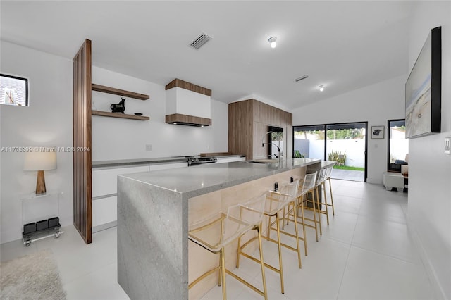 kitchen with white cabinets, sink, light stone countertops, an island with sink, and a breakfast bar area