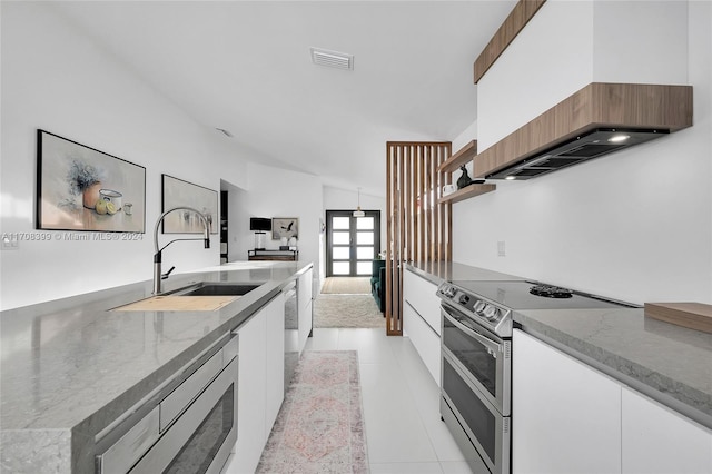 kitchen featuring light stone countertops, premium range hood, stainless steel appliances, sink, and white cabinets