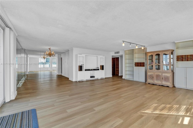 unfurnished living room with light hardwood / wood-style flooring, a textured ceiling, and an inviting chandelier