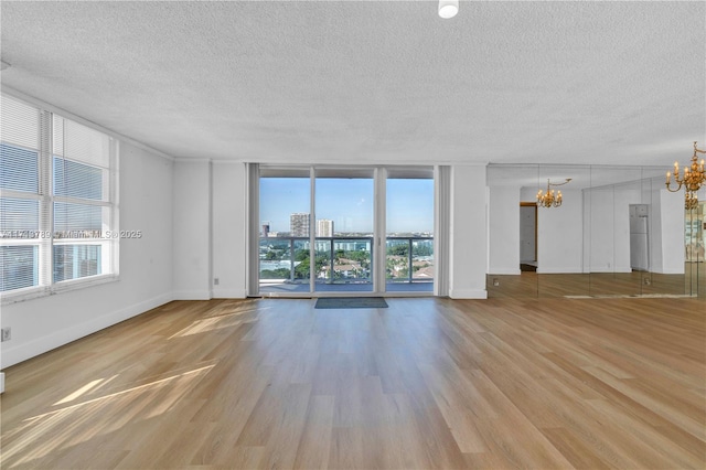 empty room with a notable chandelier, light hardwood / wood-style floors, a wall of windows, and a textured ceiling