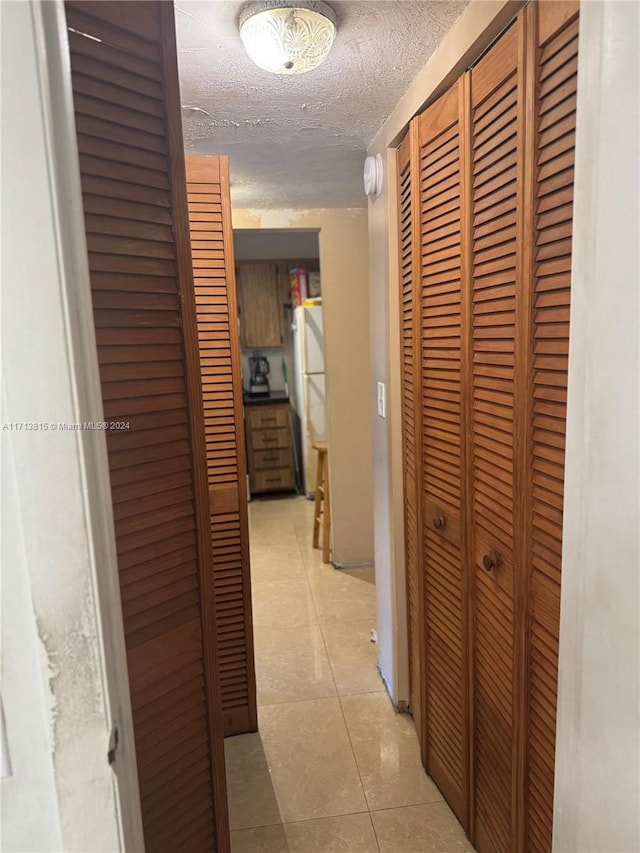 hall featuring light tile patterned floors and a textured ceiling