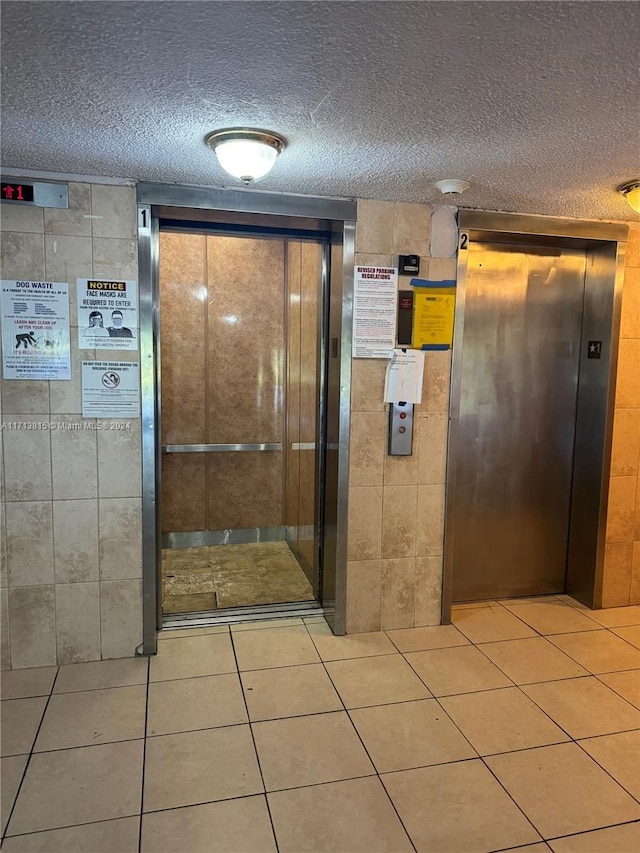 interior space with tile patterned floors, elevator, and a textured ceiling