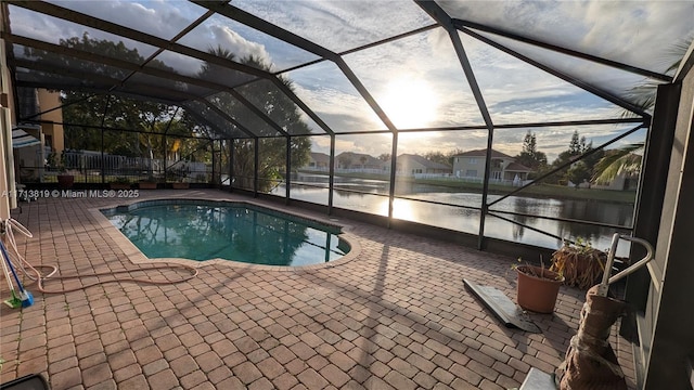 pool at dusk with a water view, a patio area, and a lanai