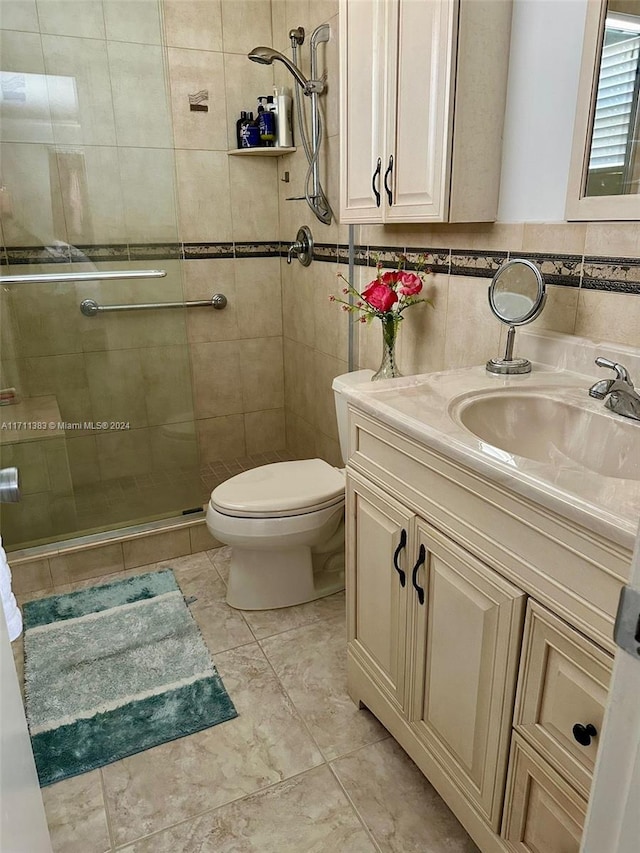 bathroom with vanity, a shower with door, tile patterned flooring, toilet, and tile walls