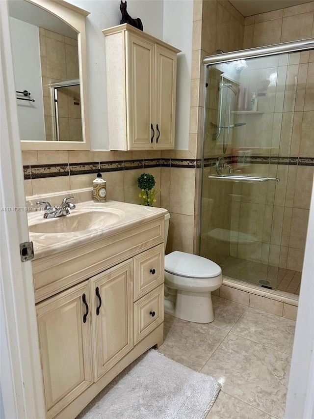 bathroom featuring tile patterned flooring, an enclosed shower, toilet, vanity, and tile walls