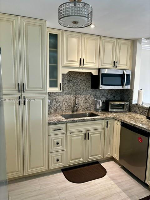 kitchen with decorative backsplash, appliances with stainless steel finishes, sink, cream cabinets, and dark stone countertops