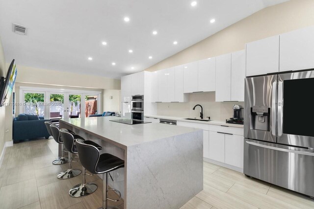 kitchen with a kitchen island, vaulted ceiling, a breakfast bar, white cabinets, and appliances with stainless steel finishes