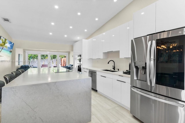 kitchen featuring lofted ceiling, appliances with stainless steel finishes, sink, and white cabinets