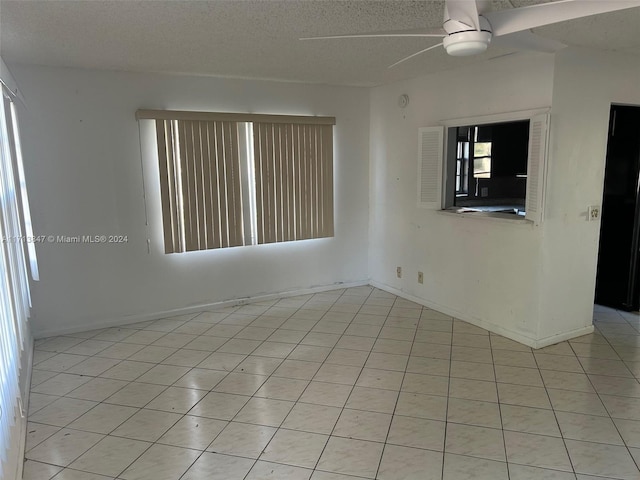 empty room with ceiling fan, light tile patterned floors, and a textured ceiling