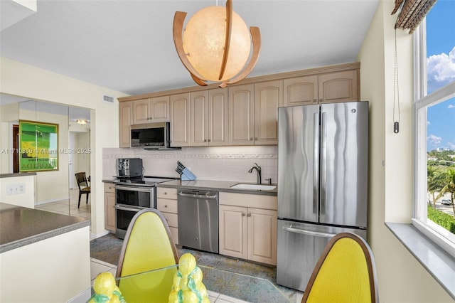 kitchen featuring sink, tasteful backsplash, light brown cabinetry, appliances with stainless steel finishes, and decorative light fixtures