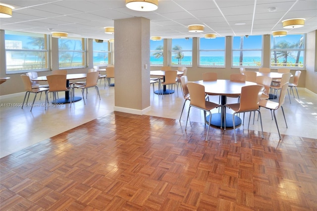 dining area featuring a drop ceiling, a water view, plenty of natural light, and parquet floors