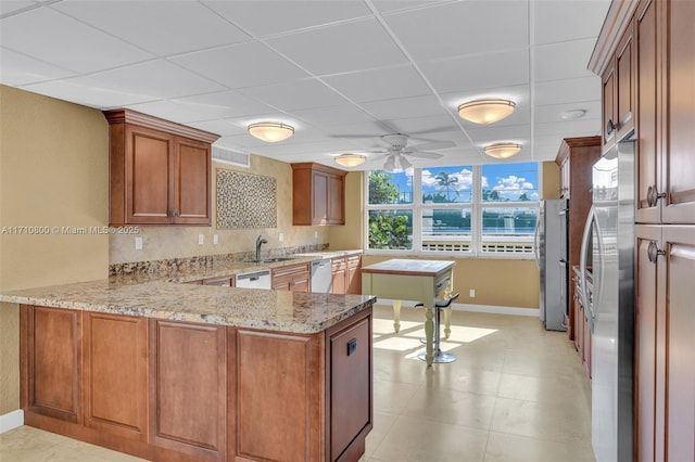 kitchen featuring kitchen peninsula, appliances with stainless steel finishes, a paneled ceiling, tasteful backsplash, and light stone counters