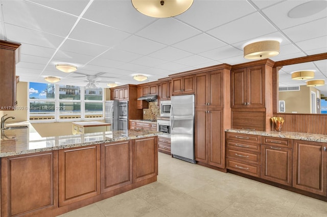 kitchen with sink, light stone counters, kitchen peninsula, a paneled ceiling, and appliances with stainless steel finishes