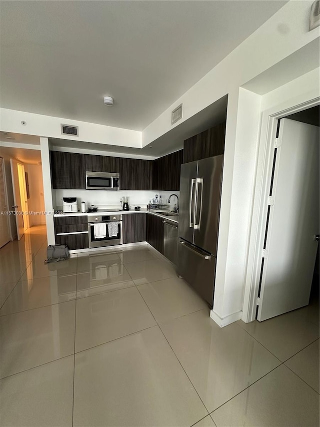 kitchen with dark brown cabinets, light tile patterned flooring, sink, and stainless steel appliances