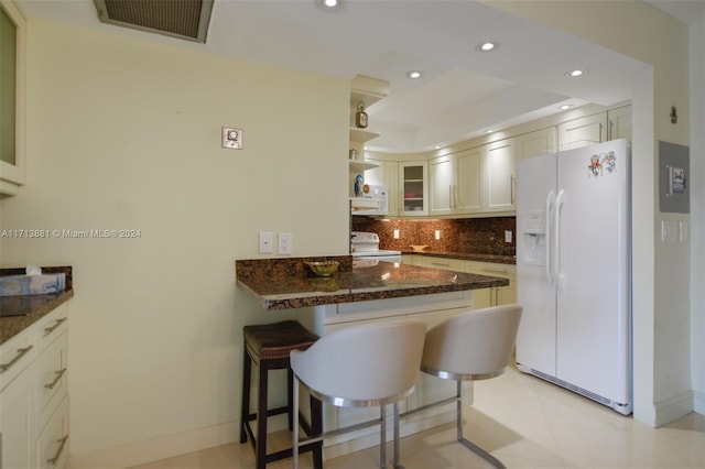 kitchen with white appliances, light tile patterned floors, dark stone countertops, white cabinetry, and a breakfast bar area