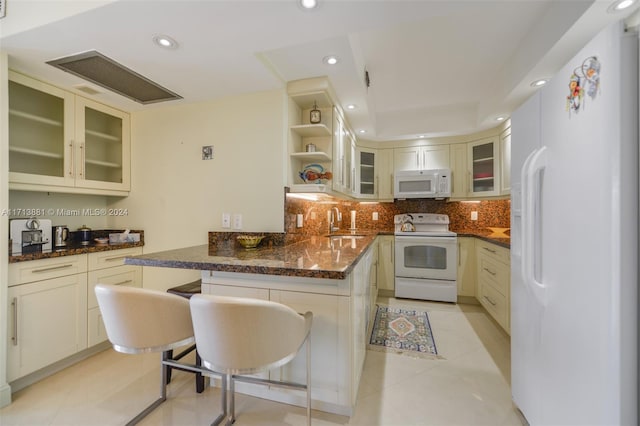 kitchen with a kitchen bar, white appliances, sink, light tile patterned floors, and dark stone countertops