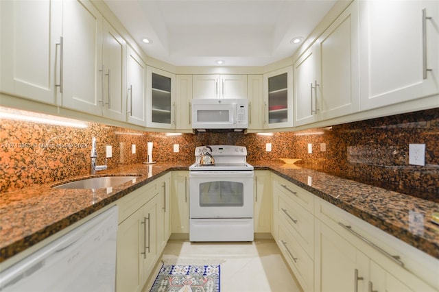 kitchen with sink, tasteful backsplash, a raised ceiling, dark stone countertops, and white appliances