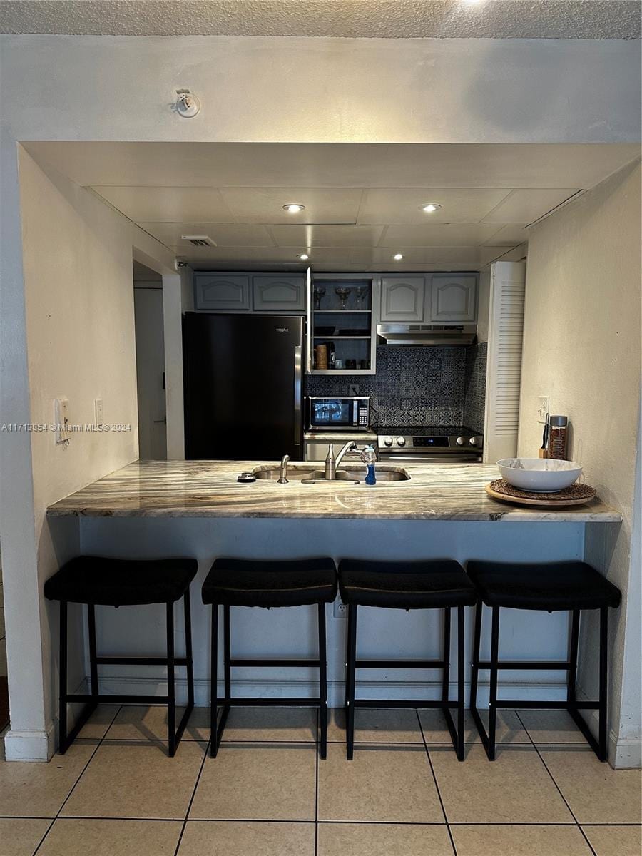 kitchen featuring decorative backsplash, refrigerator, gray cabinets, and a breakfast bar area