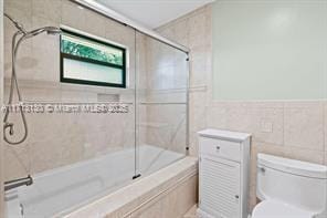 bathroom featuring tile walls, toilet, and combined bath / shower with glass door