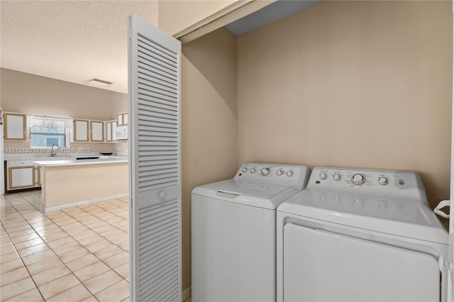 laundry area featuring light tile patterned floors, a textured ceiling, sink, and washing machine and clothes dryer