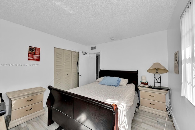 bedroom with multiple windows, a closet, light hardwood / wood-style floors, and a textured ceiling