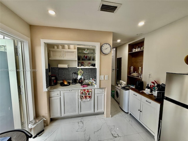 kitchen with washer and dryer, stainless steel fridge, decorative backsplash, built in shelves, and white cabinetry