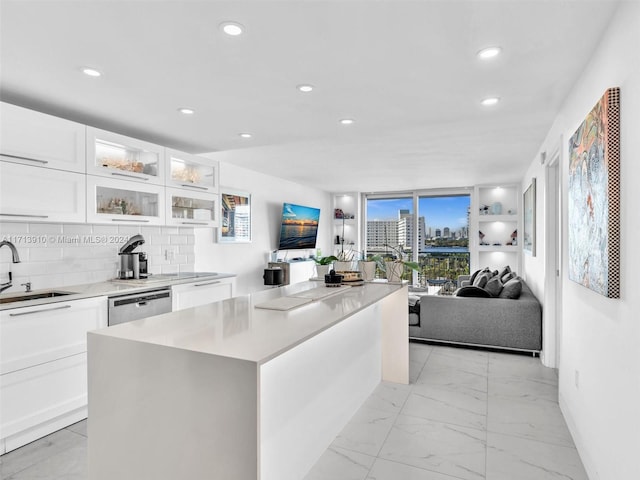 kitchen featuring a center island, sink, stainless steel dishwasher, decorative backsplash, and white cabinetry