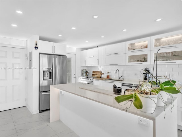 kitchen featuring light stone countertops, appliances with stainless steel finishes, backsplash, sink, and white cabinets