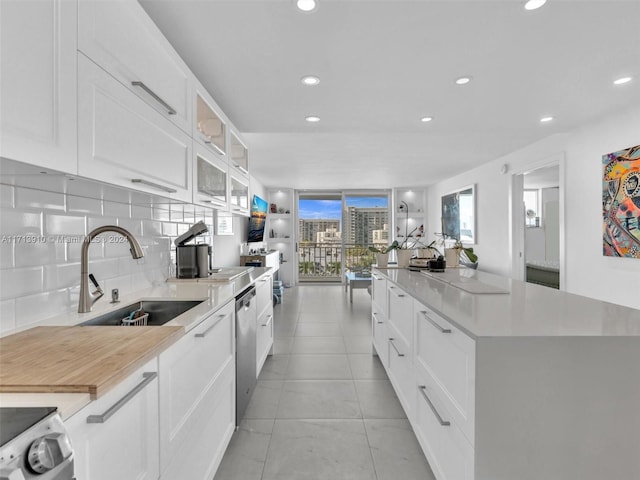 kitchen featuring stove, sink, stainless steel dishwasher, decorative backsplash, and white cabinetry