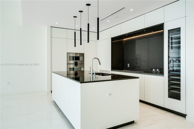 kitchen with white cabinetry, sink, hanging light fixtures, double oven, and an island with sink