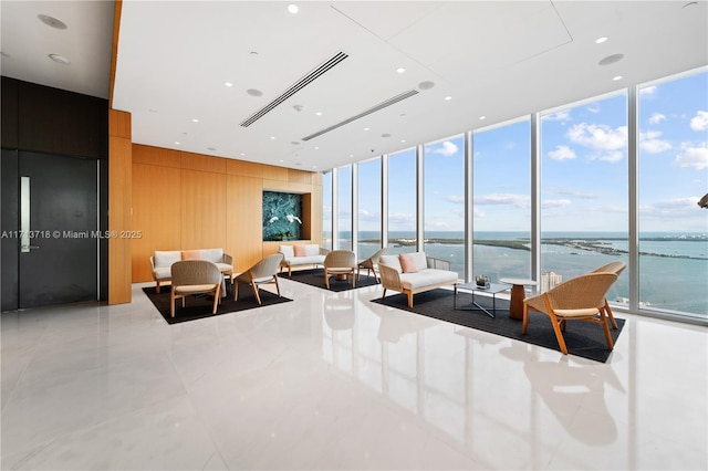 living area featuring a water view, wood walls, floor to ceiling windows, and recessed lighting