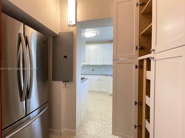 kitchen featuring white cabinets, backsplash, electric panel, and stainless steel refrigerator