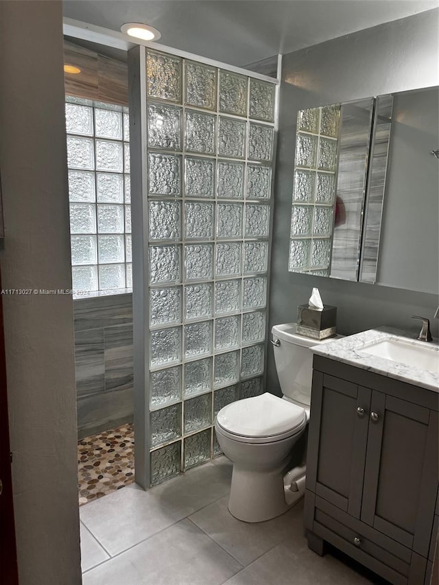 bathroom featuring tile patterned floors, vanity, toilet, and a tile shower