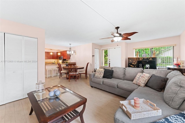 living room with ceiling fan with notable chandelier, light hardwood / wood-style floors, and plenty of natural light