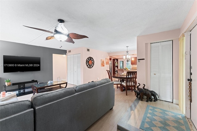 living room featuring light wood-type flooring, a textured ceiling, and ceiling fan with notable chandelier