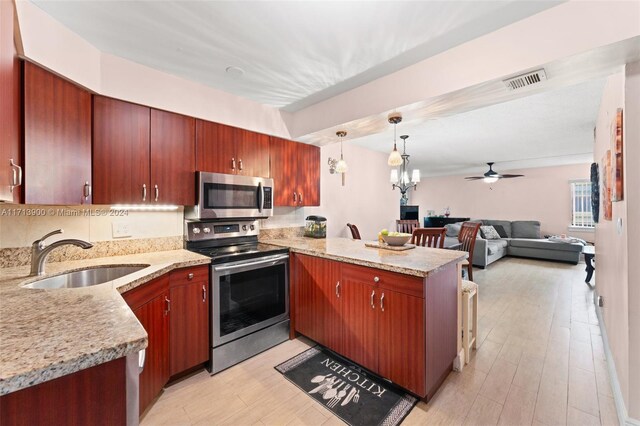 kitchen with kitchen peninsula, appliances with stainless steel finishes, ceiling fan with notable chandelier, sink, and pendant lighting