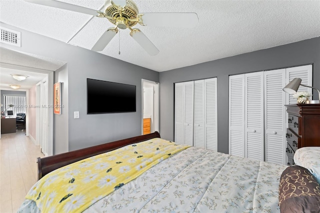 bedroom featuring hardwood / wood-style flooring, ceiling fan, a textured ceiling, and multiple closets