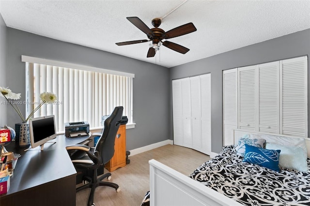 bedroom with ceiling fan, light hardwood / wood-style floors, a textured ceiling, and two closets