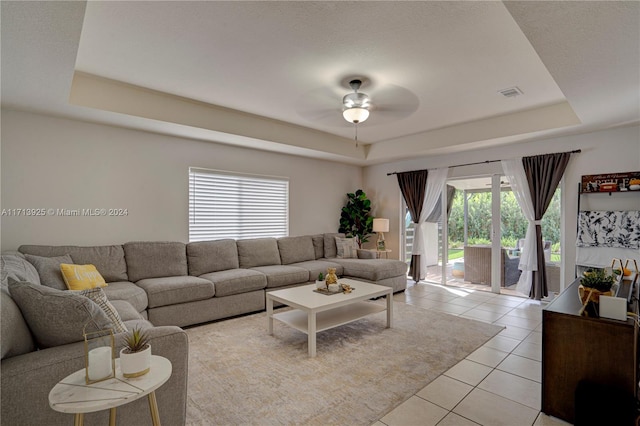 living room featuring light tile patterned floors, a raised ceiling, a wealth of natural light, and ceiling fan