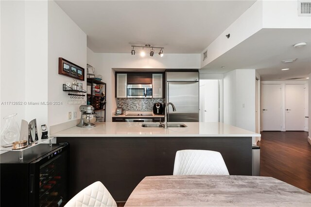 kitchen with kitchen peninsula, decorative backsplash, stainless steel appliances, beverage cooler, and sink