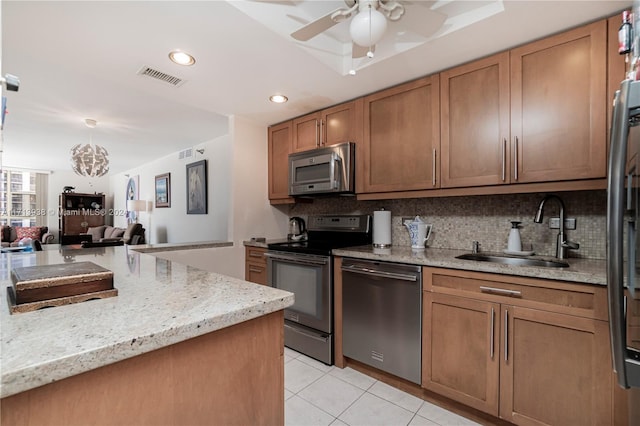 kitchen with light stone countertops, sink, stainless steel appliances, backsplash, and ceiling fan with notable chandelier