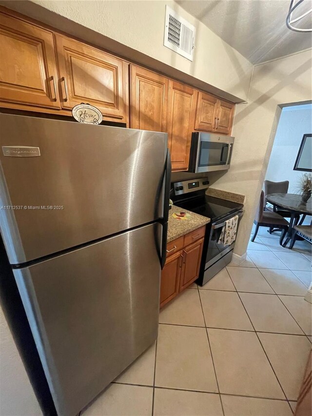 kitchen featuring light tile patterned floors, stainless steel appliances, and light stone countertops